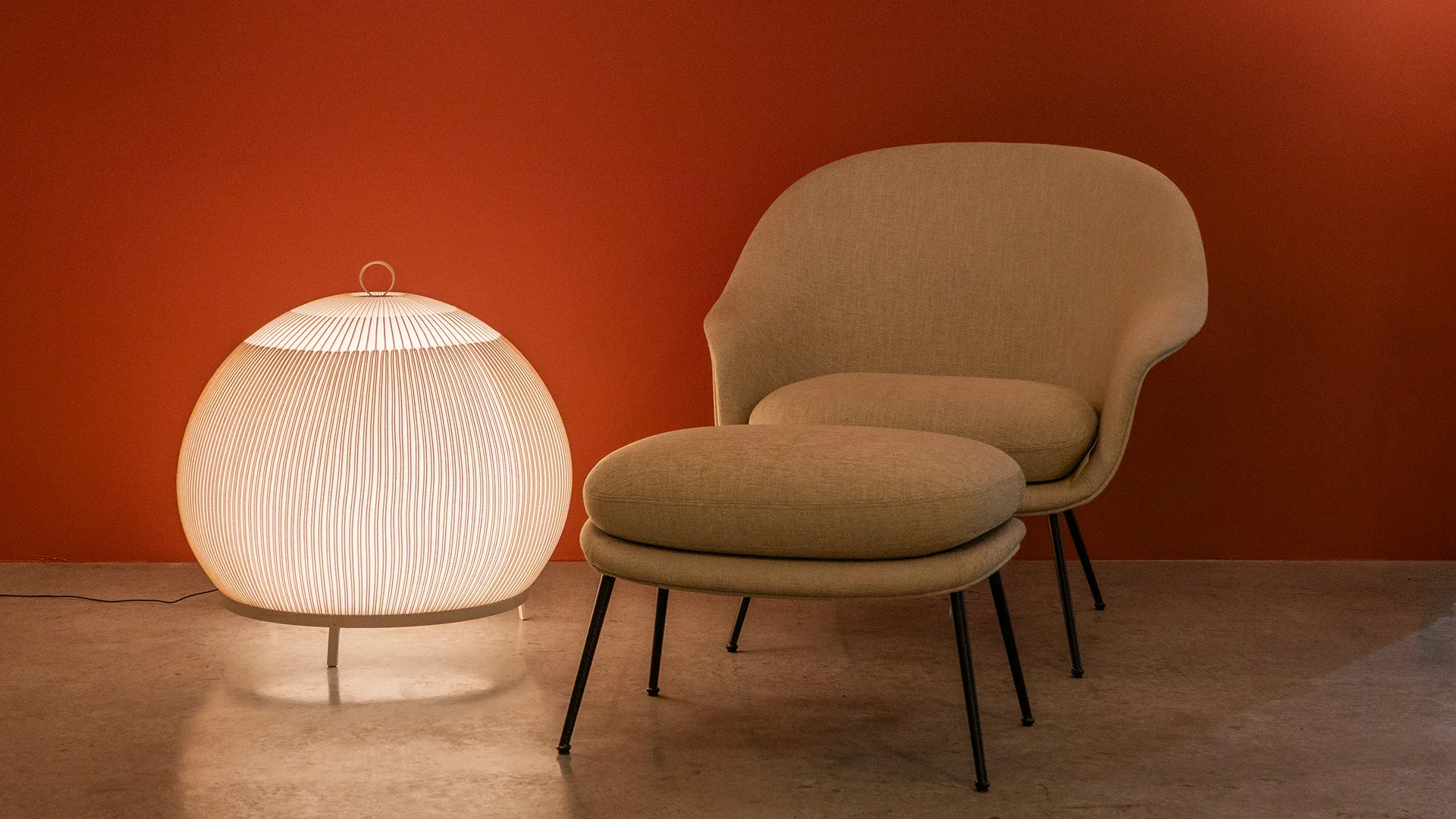 Kugelförmige Leuchte neben Sessel und Hocker vor roter Wand – Lichtstudio Weiler, Conceptlicht
