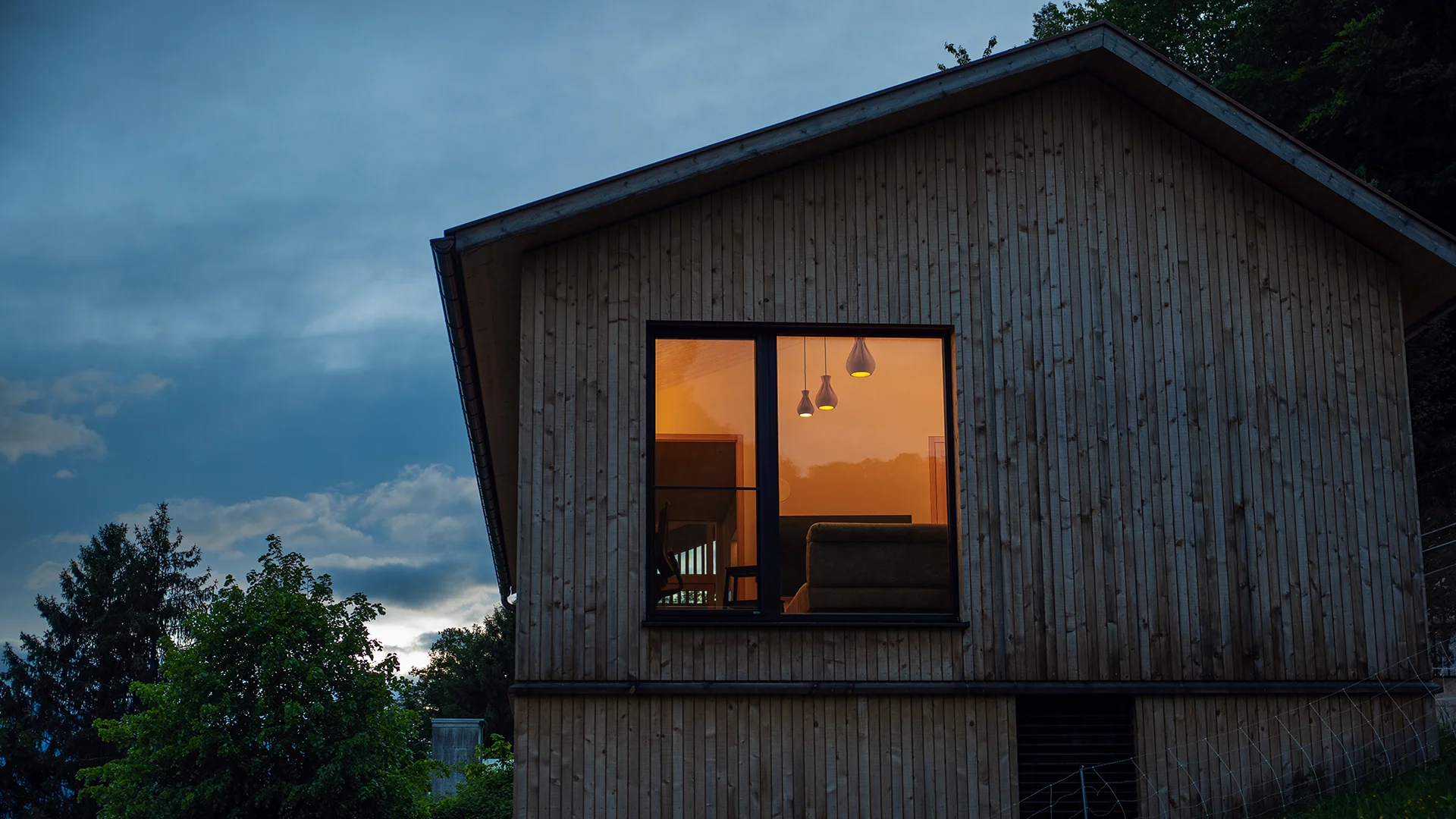 Außenansicht in der Dämmerung mit warm beleuchtetem Wohnraum – Holzhaus im Rheintal, Conceptlicht
