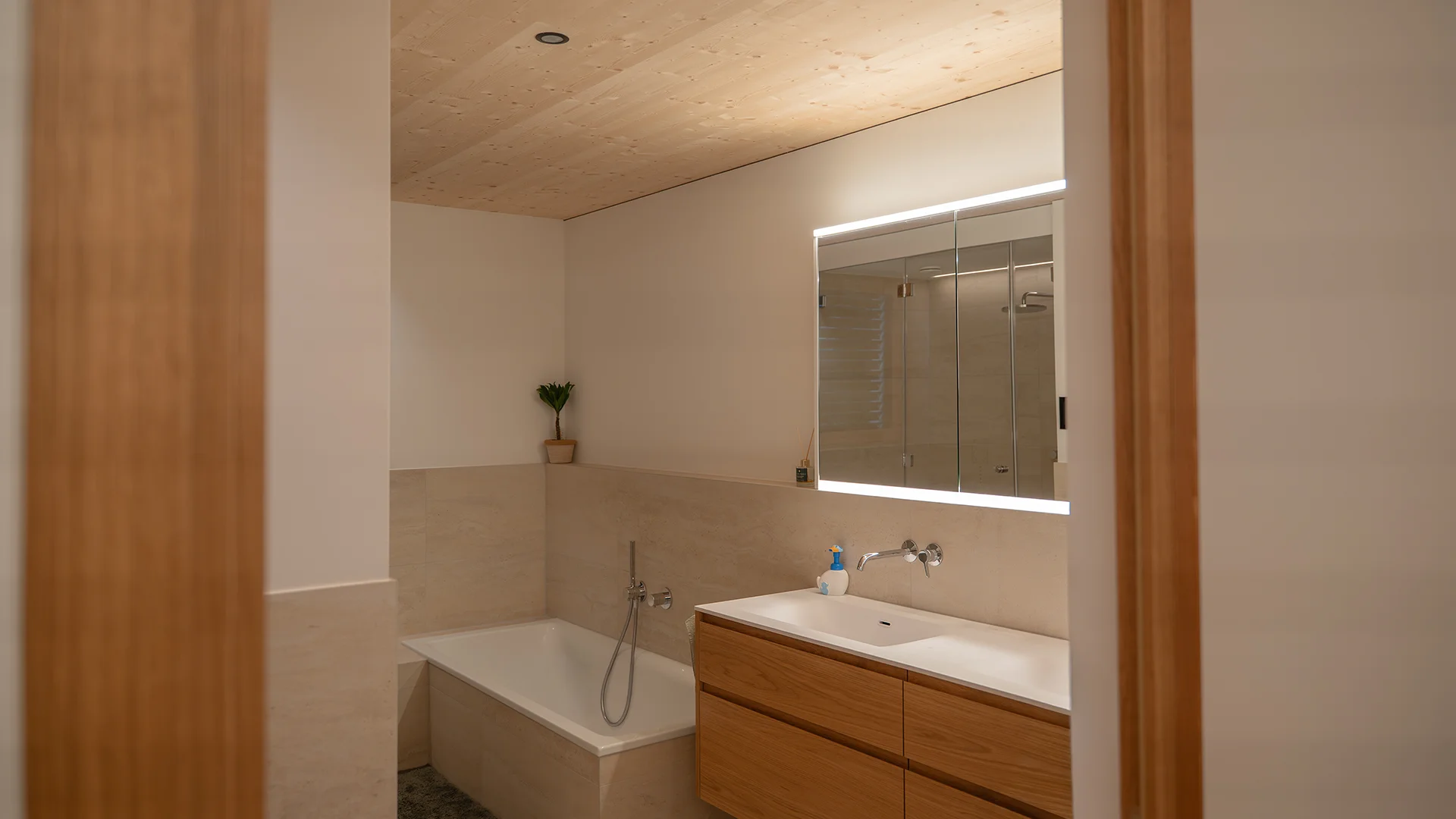 Badezimmer mit hinterleuchtetem Spiegel über dem Waschtisch – Holzhaus im Rheintal, Conceptlicht