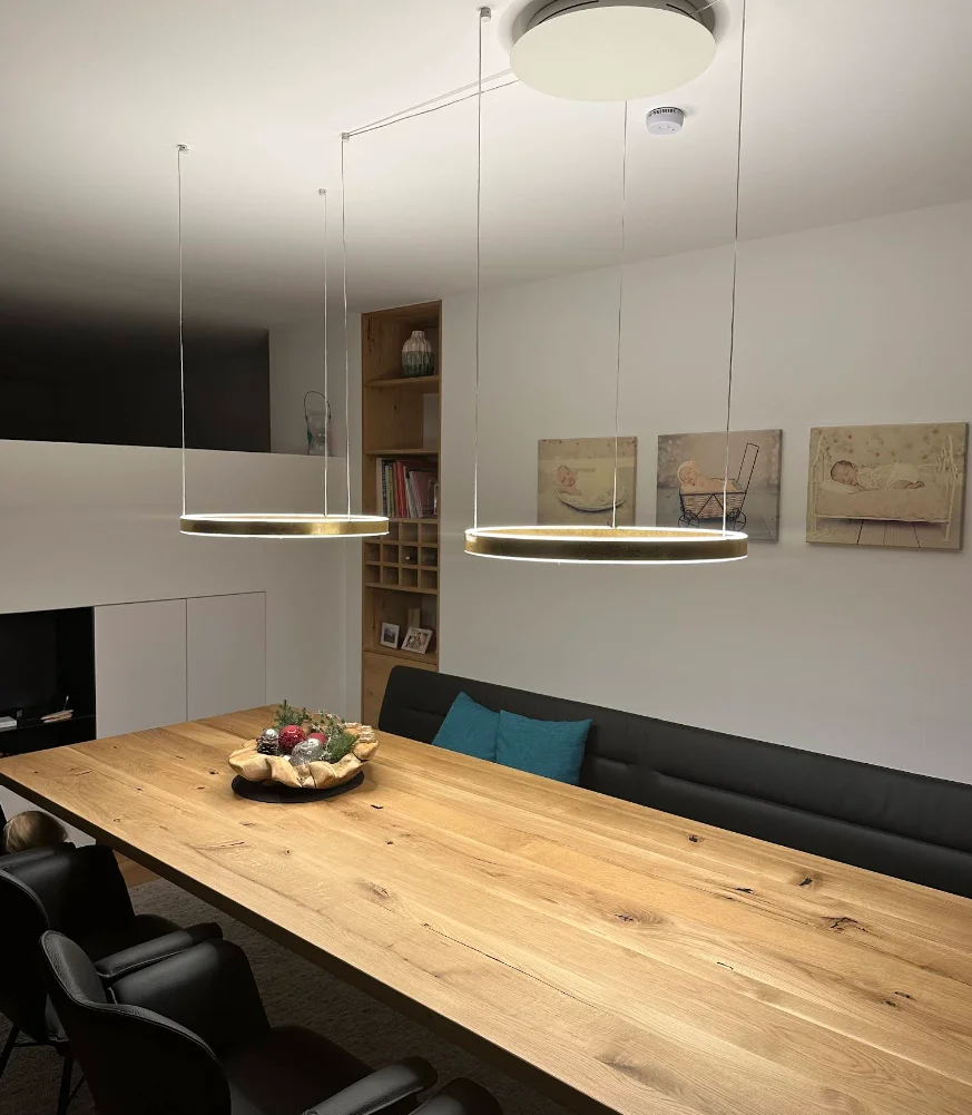 Zwei ringförmige Pendelleuchten über einem langen Holztisch im Essbereich – Kundenprojekt, Conceptlicht