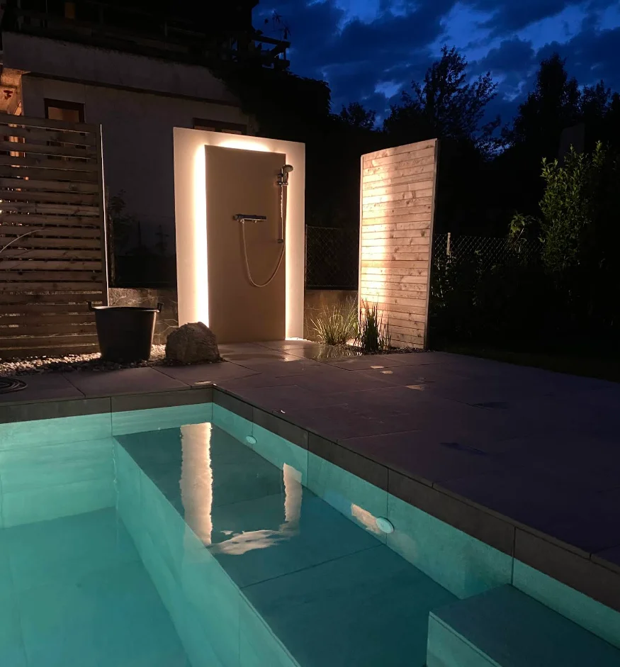 Beleuchtete Außendusche und Holzwände an einem Pool in der Abenddämmerung – Kundenprojekt, Conceptlicht