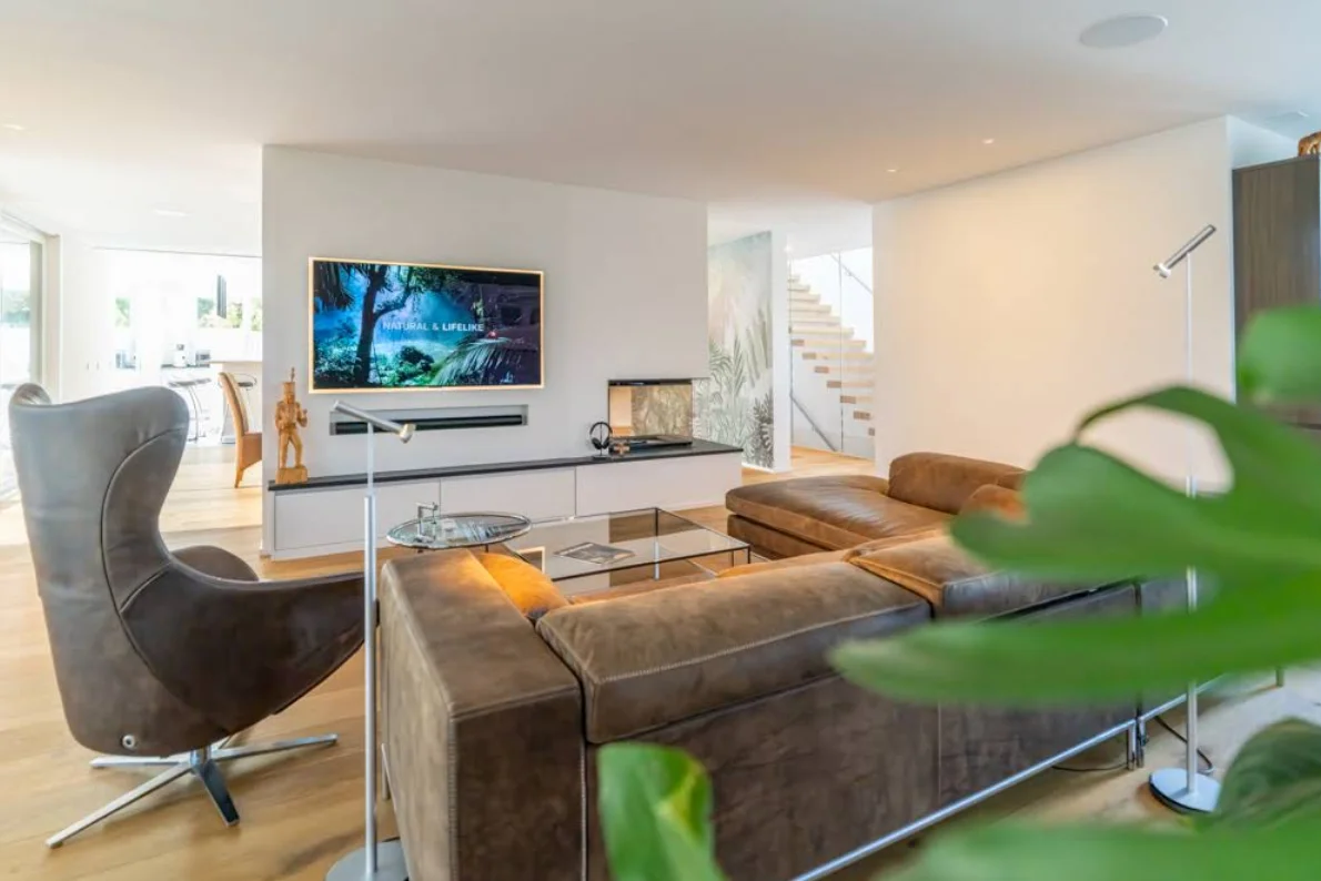 Wohnraum mit Ledersofa, Sessel und Stehleuchte neben offener Küche – Neubau, Conceptlicht